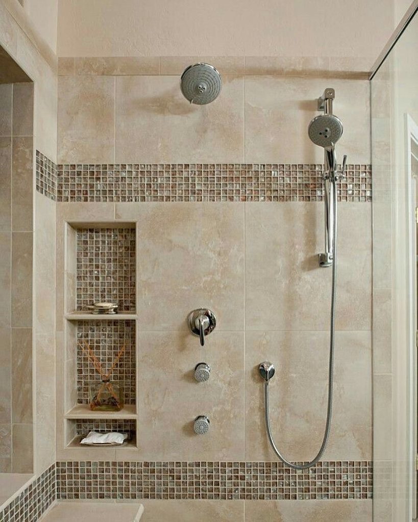 Beige-tiled shower with built-in shelves, mosaic tile accents, a handheld showerhead, and a wall-mounted faucet.