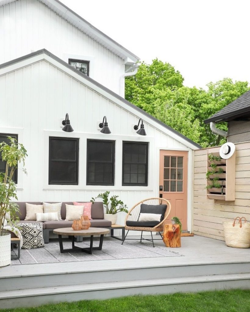 Modern patio with outdoor seating, a peach door, wall lights, plants, and a light wood privacy fence.