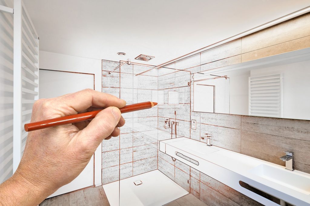 A hand sketches bathroom renovation plans over a photo, blending the real and proposed designs into one image.
