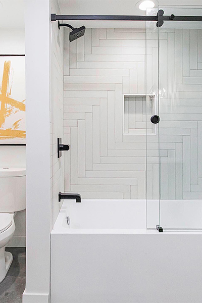 Beautiful modern remodeled bathroom with white tiling, black finish, and glass doors