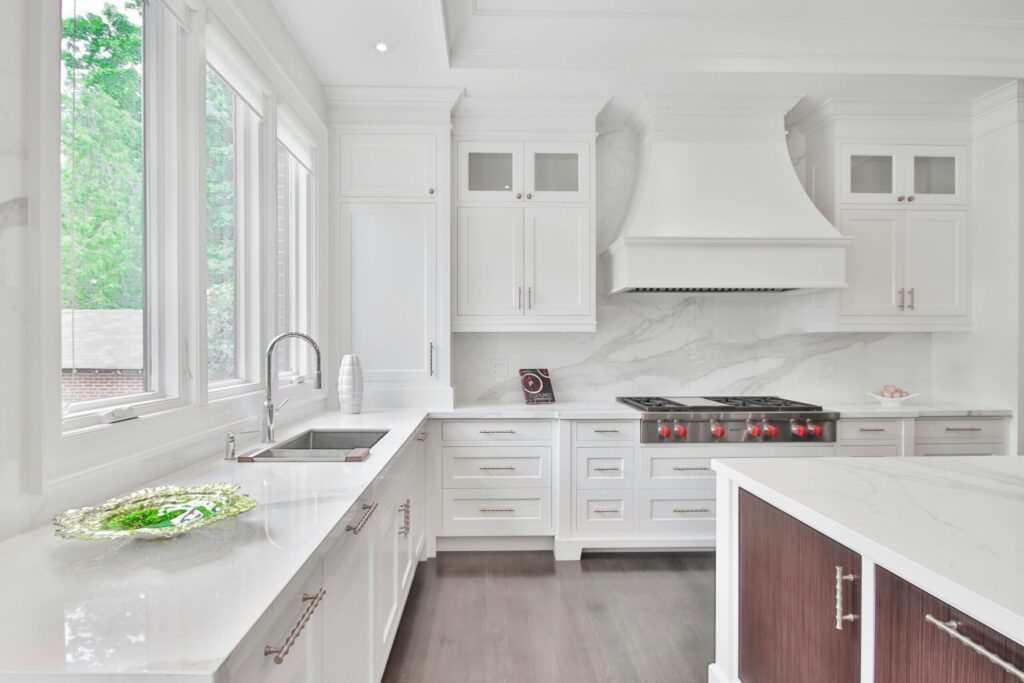 Modern kitchen with white cabinets, marble countertops, large windows, and a stove with a white range hood.